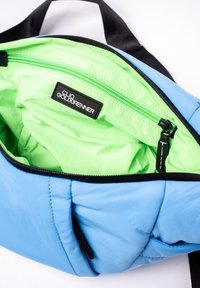 Sac bleu clair avec une finition lisse et matelassée. L'intérieur est orné d'une doublure verte vibrante et d'une poche zippée noire avec étiquette de marque.