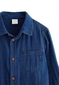 Camicia in denim di colore blu scuro con taschino frontale, chiusura a bottoni e colletto classico. Presenta bottoni marroni e cuciture a contrasto.