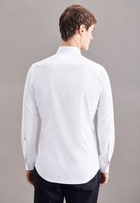 Weißes Langarmhemd aus glattem Stoff, mit Rückenpasse, abgerundetem Saum und Ein-Knopf-Manschetten, von hinten betrachtet.