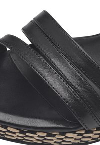 Sandal in pelle nera caratterizzata da tre ampie cinghie, una soletta testurizzata e una suola intermedia in materiale naturale intrecciato.