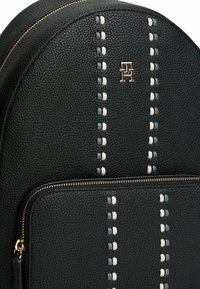 Mochila de cuero negro con forma redondeada, cremallera en tono dorado y costuras decorativas en gris y crema en la parte frontal.