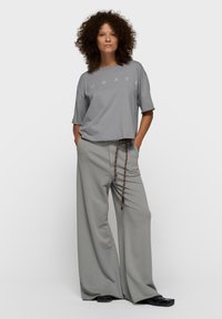 T-shirt gris court avec le texte "DAYS", assorti à un pantalon large gris clair avec une taille à cordon de serrage aux accents marron et noir contrastés.