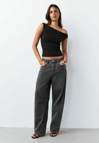 Čierny priliehavý top s odhalenými ramenami v kombinácii s voľnými tmavosivými džínsami s vysokým pásom, ktoré majú predné vrecká a jemné švové detaily.