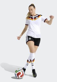 White soccer jersey with black and red accents, featuring a geometric pattern, paired with black shorts and knee-high white socks displaying a design.
