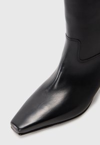 Crne kožne čizme do gležnja, špičasti vrh, glatka tekstura, minimalni šavovi, elegantan dizajn, visoka potpetica, otkriva dio gornjeg dijela čizme.