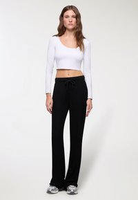 Crop top bianco a maniche lunghe e pantaloni neri a gamba larga realizzati in tessuto morbido. I pantaloni presentano una vita con coulisse e una vestibilità rilassata. Sneakers argentate.