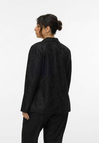 Zwarte blazer met een gestructureerd bloemenpatroon, enkele achtersplit, notch revers en met knopen afgewerkte manchetten, gestyled met bijpassende broeken.