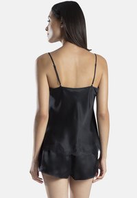 Camisole en satin noir avec des bretelles fines réglables et une bordure en dentelle festonnée à l'ourlet, associée à un short assorti. Texture lisse.