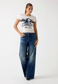 Cropped white t-shirt with navy graphic print, paired with high-waisted wide-leg jeans in dark blue denim. Smooth texture, casual fit.