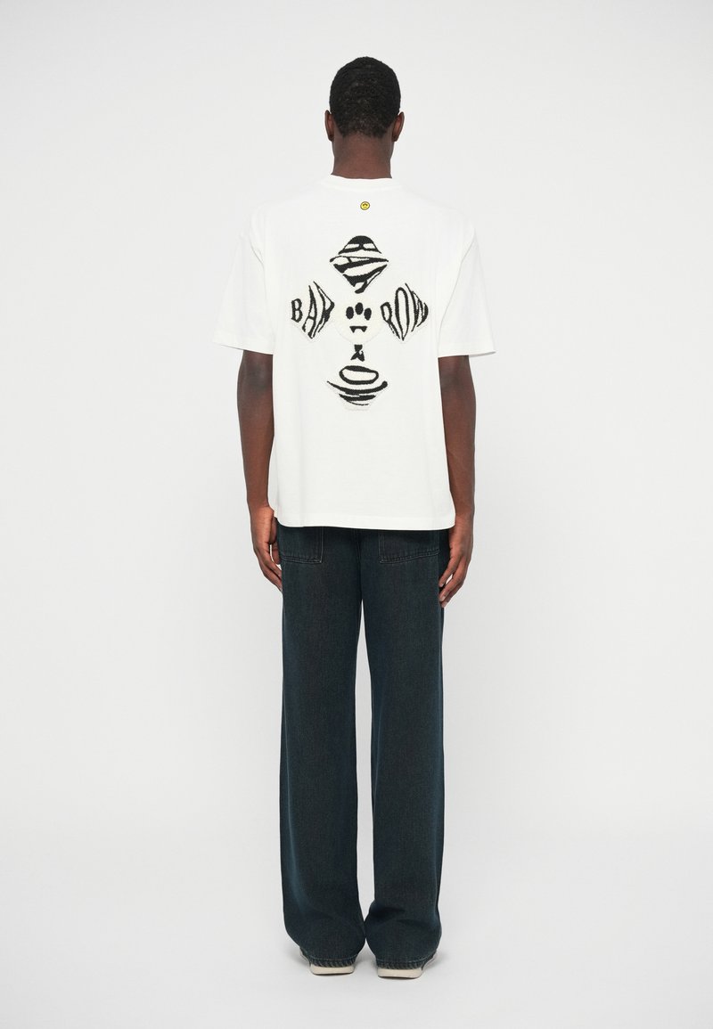 Λευκό βαμβακερόT-shirt με μαύρο αφηρημένο γραφικό σχέδιο στο πίσω μέρος. Σε συνδυασμό με σκούρες φαρδιές τζιν παντελόνες. Λείος υφής.