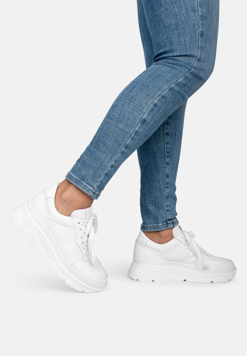 White sneakers with a textured leather upper, rounded toe, and thick soles. Laces are tied, and sneakers have subtle stitching details.