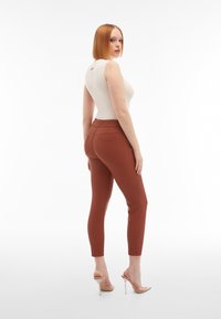 Top de crema ajustado y sin mangas combinado con leggings de tiro alto en color óxido. Los leggings cuentan con bolsillos en la parte posterior y una textura suave y elástica.