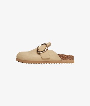 Beige slip-on mule made of soft suede, featuring a decorative metal buckle and a textured cork accent on the sole. Flat, rubber outsole.