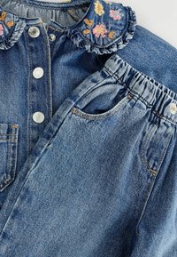 Setelan denim yang menampilkan atasan kancing dengan kerah bordir bunga dan sepasang celana elastis dengan saku samping.