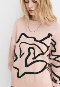 Maglione rosa chiaro con audace motivo astratto nero, scollatura rotonda e orlo a coste. Tessuto a maglia con una texture morbida.