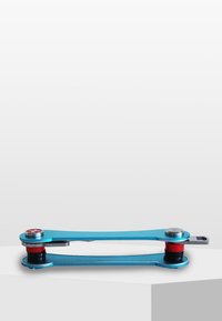 Blå metallmultiverktyg med en avlång form, med cirkulära röda och silverfärgade accenter i varje ände. Slät yta och minimal design.