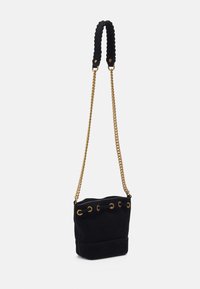 Bolso de cubo de ante negro con un asa trenzada y una correa de cadena dorada, que presenta ojales de metal en la parte superior y un cuerpo de textura suave.