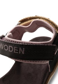 Svarta sandaler med ett rosa vadderat rem, featuring en texturerad svart logotyp och en beige korkdetalj. Mjuk mockainsida ger komfort.