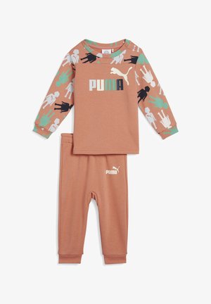 Světle hnědý dvoudílný outfit skládající se z topu s dlouhým rukávem, který má barevný vzor a logo, a k tomu odpovídající kalhoty na gumu.