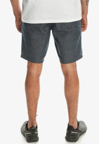 Mörkblå denimshorts med en strukturerad yta, med rak skärning och en något ovanför knäet-längd. Bärs med svarta sportskor.