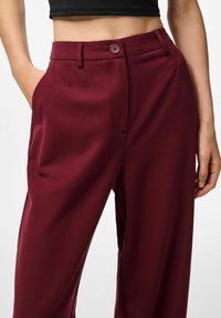Burgundy vida byxor med vida ben, tillverkade av ett mjukt tyg, med en framficka, sned design och tvåknappslås i midjan.