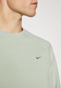 Felpa verde chiaro con scollo rotondo. Presenta un logo Nike verde scuro sul petto. Realizzata in tessuto morbido e liscio, con dettagli a costine.
