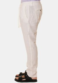 Pantaloni in lino color beige chiaro con vestibilità rilassata, caratterizzati da pieghe frontali, tasche laterali e una vita con cordoncino per una regolazione ottimale.