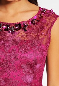 Fuchsiové krajkové šaty s květinovým vzorem; zdobený výstřih s flitry a korálky. Bezramenný design s přiléhavým střihem.