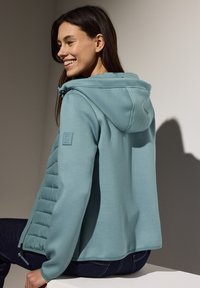 Giacca a vento blu chiaro con un frontale trapuntato e testurizzato. Presenta una patch del logo sulla manica. Tessuto liscio con una vestibilità comoda.