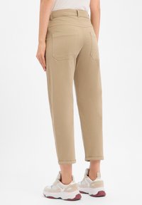 Pantalon beige taille haute à coupe décontractée, avec poches arrière et revers roulés, associé à des baskets claires. Tissu lisse et robuste.