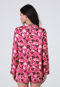 Completo pigiama floreale con finitura in raso, base rosa vivace e motivi floreali scuri. Maniche corte e pantaloni corti, con dettagli in piping bianco.
