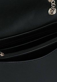 Borsa a mano in sintetico nero con una texture liscia, dotata di un comparto con zip e accentuata da una catena dorata. La parte superiore aperta rivela tasche interne.