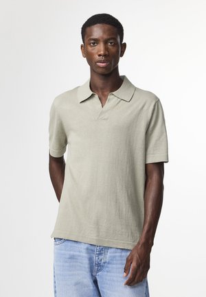 Kortärmad polo i ljusgrön, tillverkad av mjukt material. Har en krage och en avslappnad passform, i kombination med blå denim.