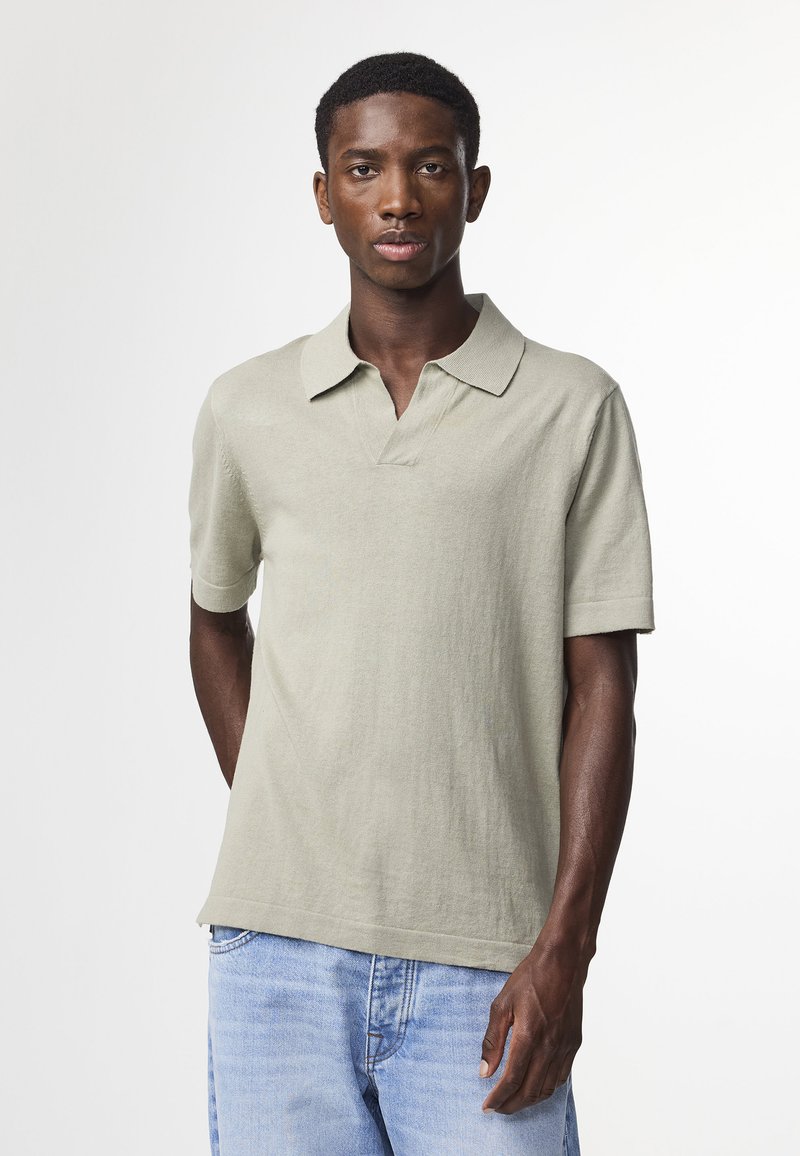 Polo a maniche corte in verde chiaro, realizzato in materiale morbido. Presenta un colletto e una vestibilità comoda, abbinato a jeans blu.