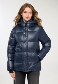 Giacca imbottita blu navy con finitura lucida, forma oversize, cappuccio con coulisse e chiusura con bottoni. Presenta sezioni trapuntate e tasche laterali.