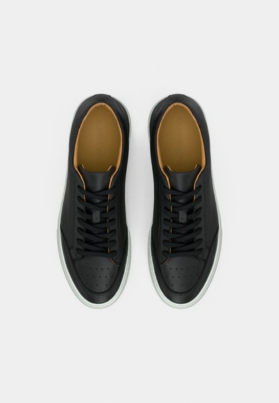 Ζευγάρι μαύρα δερμάτινα sneakers με μαύρα κορδόνια και ταμπά εσωτερική επένδυση, σε θέα από πάνω σε λευκό φόντο.