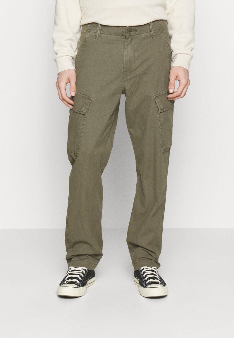 Pantalones cargo de color verde olivo hechos de algodón, con dos grandes bolsillos laterales, un diseño de pierna recta y cierre de botón. Combinados con zapatillas negras.