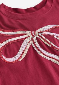 Vinröd t-shirt med en stor bågdesign i paljetter i vitt, rosa och röd. Slät textur med rund halsringning.