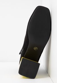 Chaussure pour femme en daim noir à talon haut carré, semelle en caoutchouc texturée, avec un accent doré à la base du talon. Taille 37.