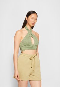 Top halter cropped verde claro com um recorte em forma de olho, combinada com calções beges com cintura elástica e detalhe de laço.