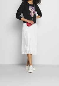 Sudadera negra con un gráfico de dibujos animados, falda midi blanca plisada con rayas plateadas y zapatillas blancas. Pequeño bolso cruzado rojo.