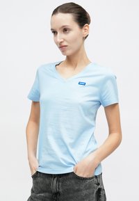 Ανοιχτό μπλε V-λαιμόκοψη T-shirt από απαλό ύφασμα, με μικρό μπλε λογότυπο "HUGO" στο αριστερό στήθος. Κοντά μανίκια και άνετη εφαρμογή.