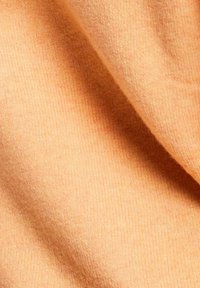 Jasnopomarańczowy materiał z miękką, dzianinową teksturą; charakteryzuje się pionowym prążkowaniem i lekkiym połyskiem; dobrze układa się w fałdy.