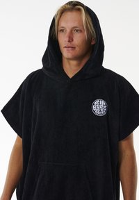 Poncho nero con cappuccio realizzato in materiale simile a asciugamano. Presenta una tasca frontale e un logo circolare sul petto. Tessuto morbido e vestibilità ampia.