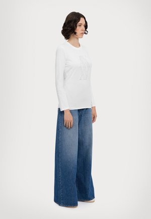 Top bianco in cotone a maniche lunghe con stampa grafica al centro, abbinato a jeans in denim blu a gamba larga con una lavatura sfumata.