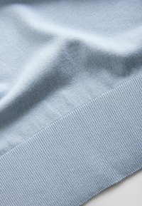 Tessuto lavorato a maglia azzurro chiaro con una fine trama a coste lungo il bordo, che mostra pieghe morbide e superficie liscia.