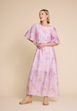 Lilla maxikjole med flagrende ærmer, prydet med et blomsterdesign i pink og grøn. Glat tekstur med en indsnævret talje, parret med beige sko.