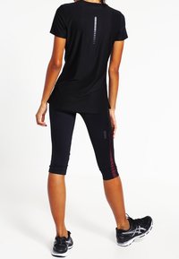 Camiseta atlética negra de manga corta con una franja vertical reflectante en la parte posterior, combinada con leggins capri negros que presentan una franja de acento burdeos.