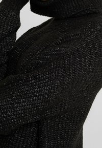 Maglione nero lavorato a maglia con colletto alto, caratterizzato da un motivo testurizzato e da un materiale morbido, che accentua calore e comfort.