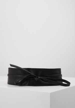 Ceinture en cuir noir avec un nœud papillon noué, présentée sur une surface blanche avec un fond uni gris clair.